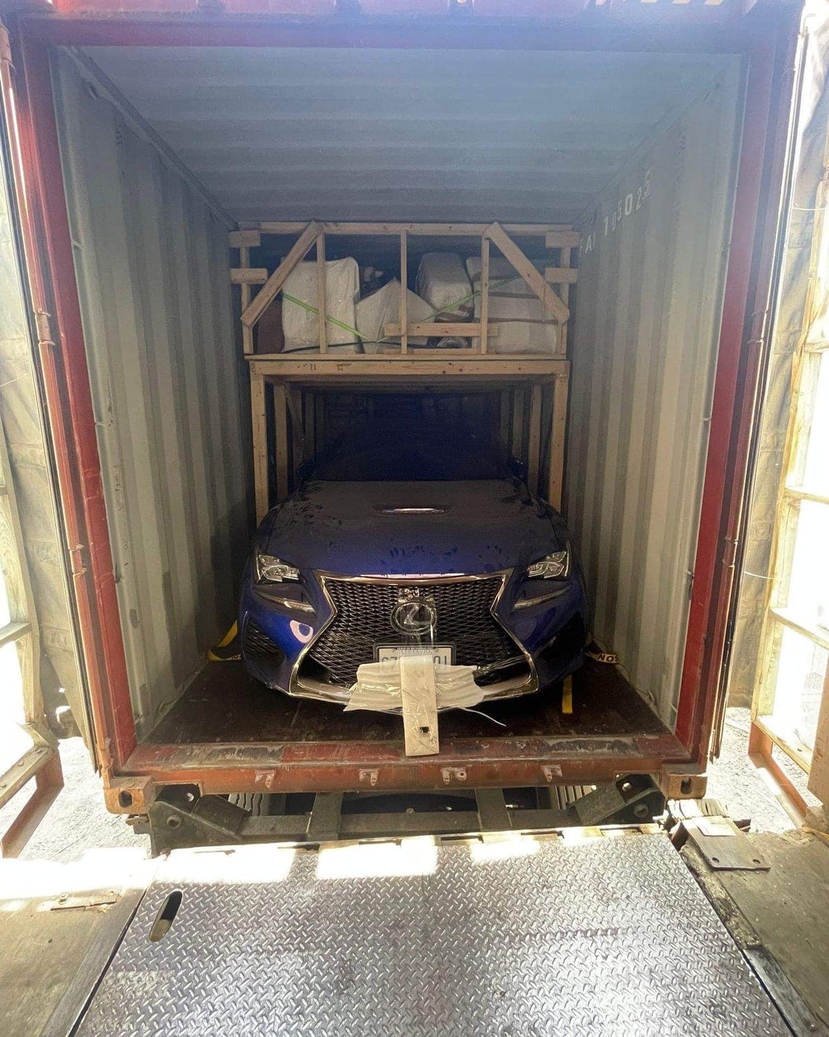 A car loaded inside a shipping container with household goods stowed on a timber deck built above it