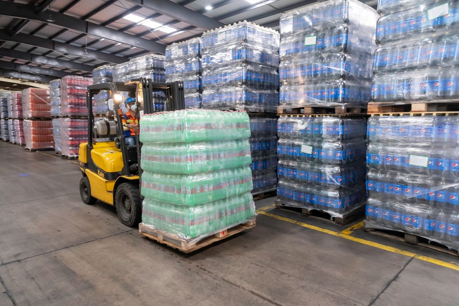 Forklift moving shrink-wrapped pallets across a warehouse floor
